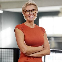 Senior woman with glasses and orange shirt smiling with arms folded