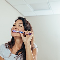 Woman in light blue shirt brushing teeth